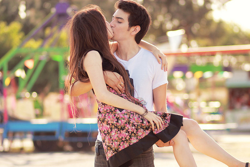 Пара в парке на закате. Парень держит девушку на руках. Она целует его. Счастье и веселье.